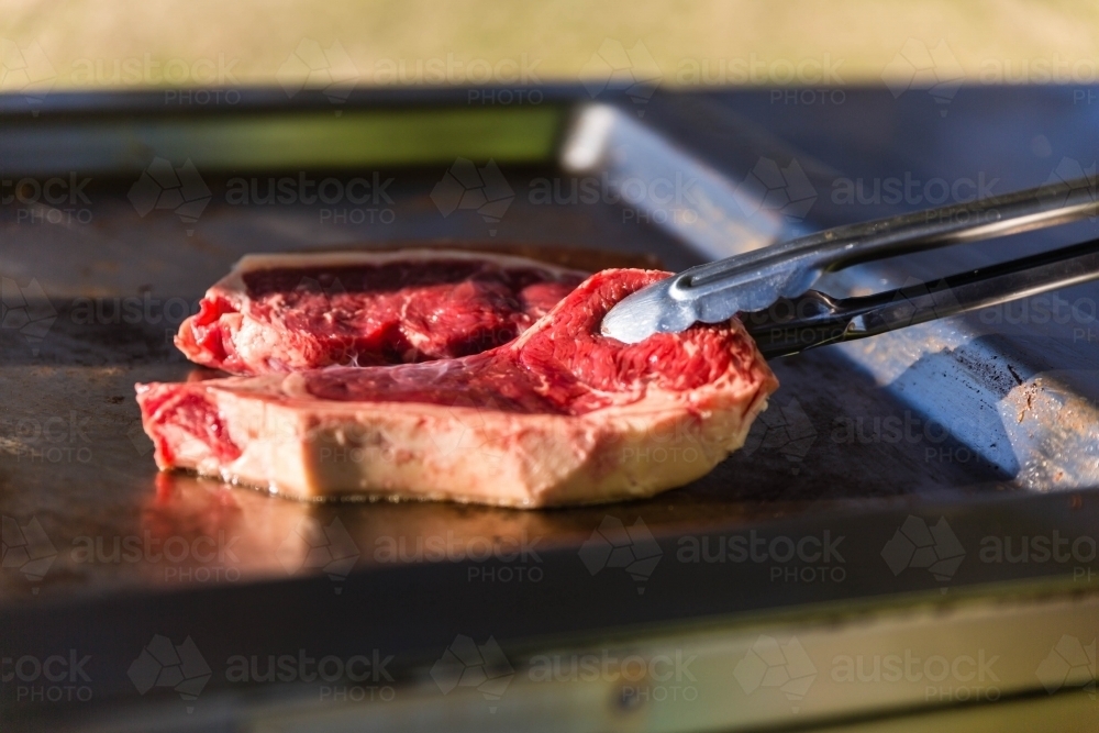 Steaks on barbecue with tongs - Australian Stock Image