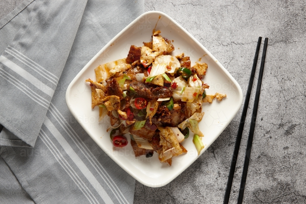 Stir fried pork slices with vegetables with black chopsticks resting on the surface counter - Australian Stock Image