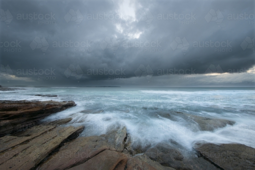 Storm over the ocean with rocks and blurred waves in foreground - Australian Stock Image