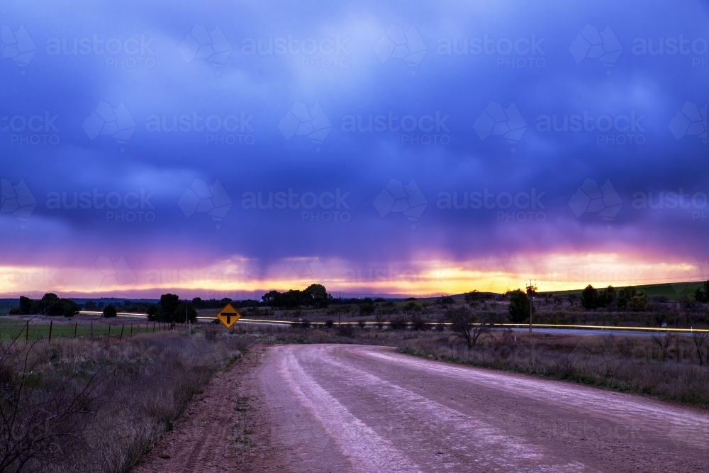 Stormy skies at sunset with car lights on road - Australian Stock Image