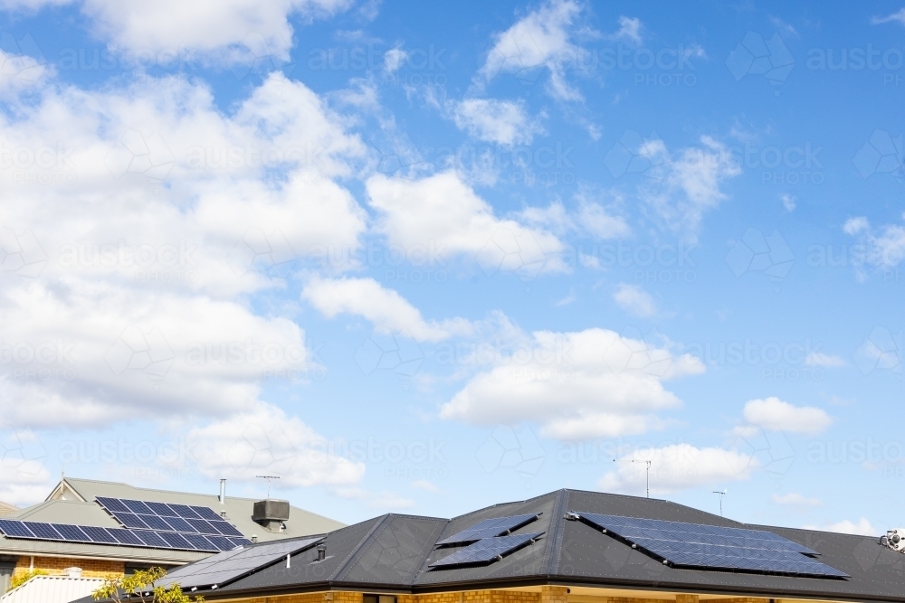 suburban roofs with solar panels under a blue sky with clouds - Australian Stock Image