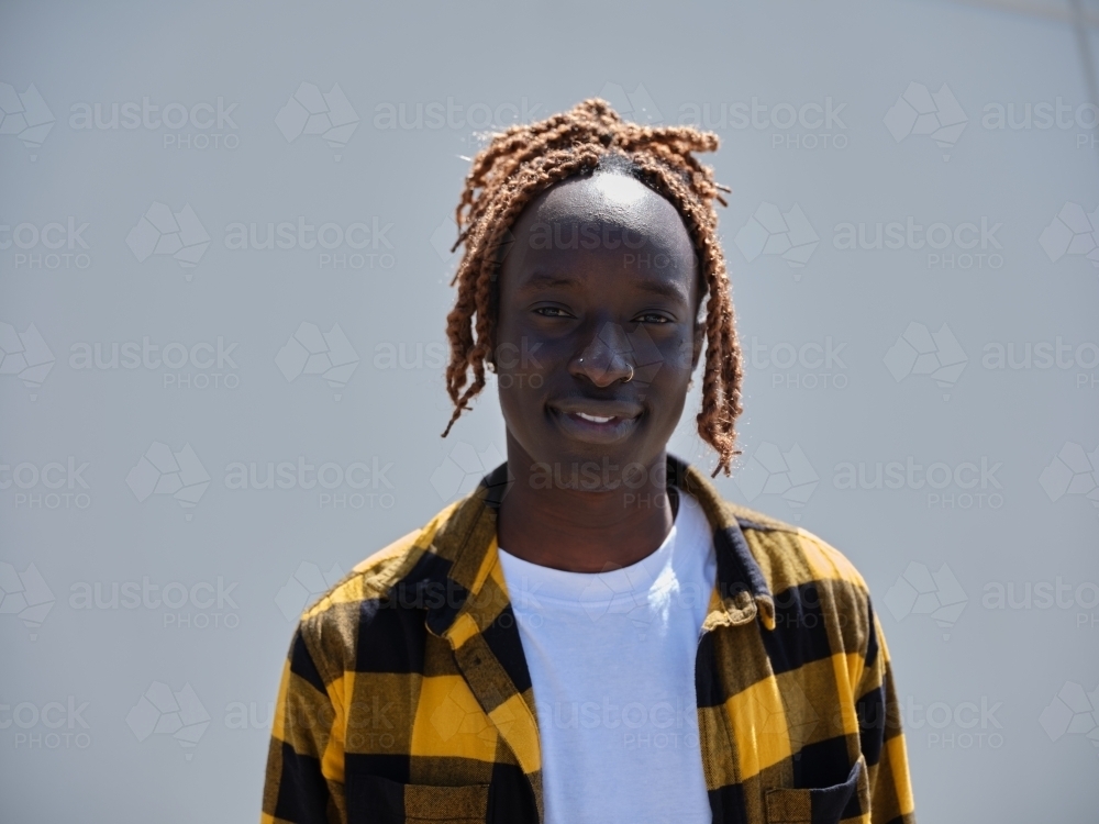 Sudanese man wearing a yellow flannel standing against a blank wall - Australian Stock Image