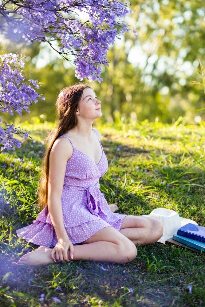 Summer scene of teen girl sitting on grassy slope relaxing outside - Australian Stock Image