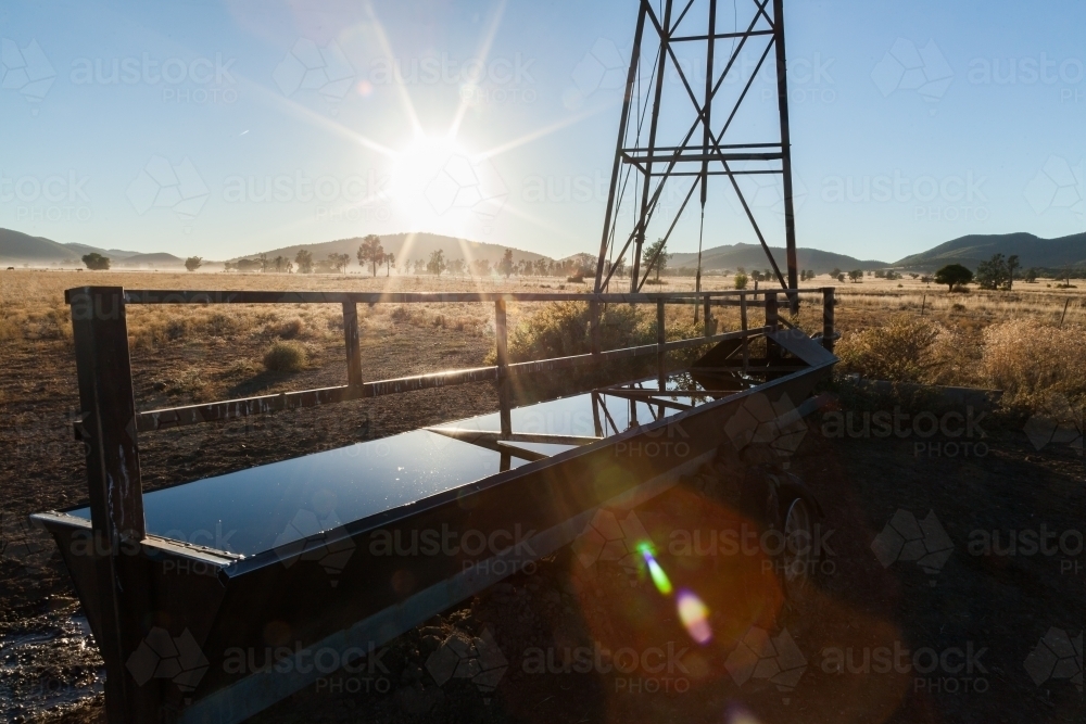 Sun flare over water trough on farm with windmill - Australian Stock Image