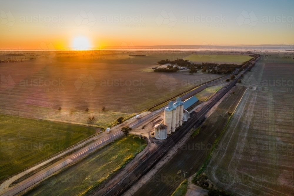 Sun rising in the distance with fields and silos in the foreground - Australian Stock Image