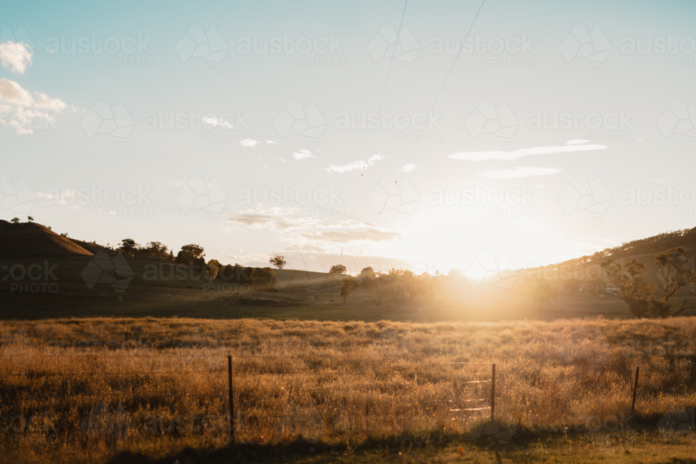 Sun setting behind distant hills in rural Australian countryside - Australian Stock Image
