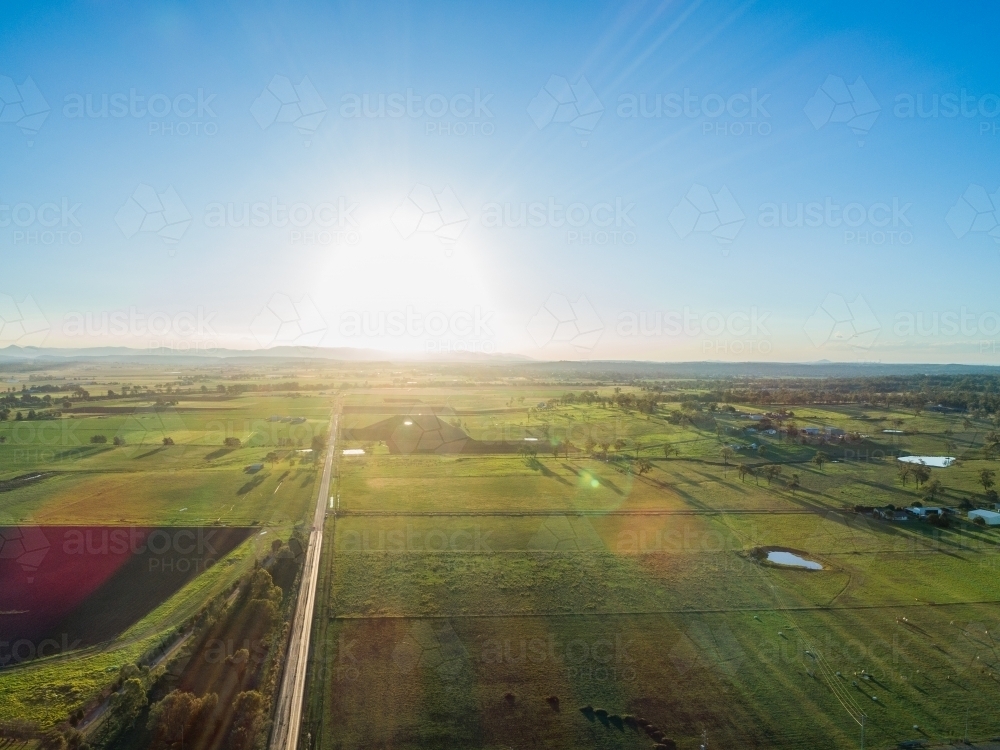 Sun setting in blue sky over rural Australian agricultural landscape - Australian Stock Image