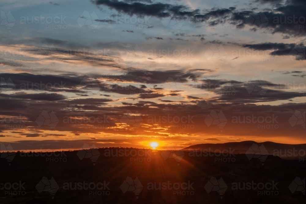 Sun setting in cloudy sky over rural landscape - Australian Stock Image