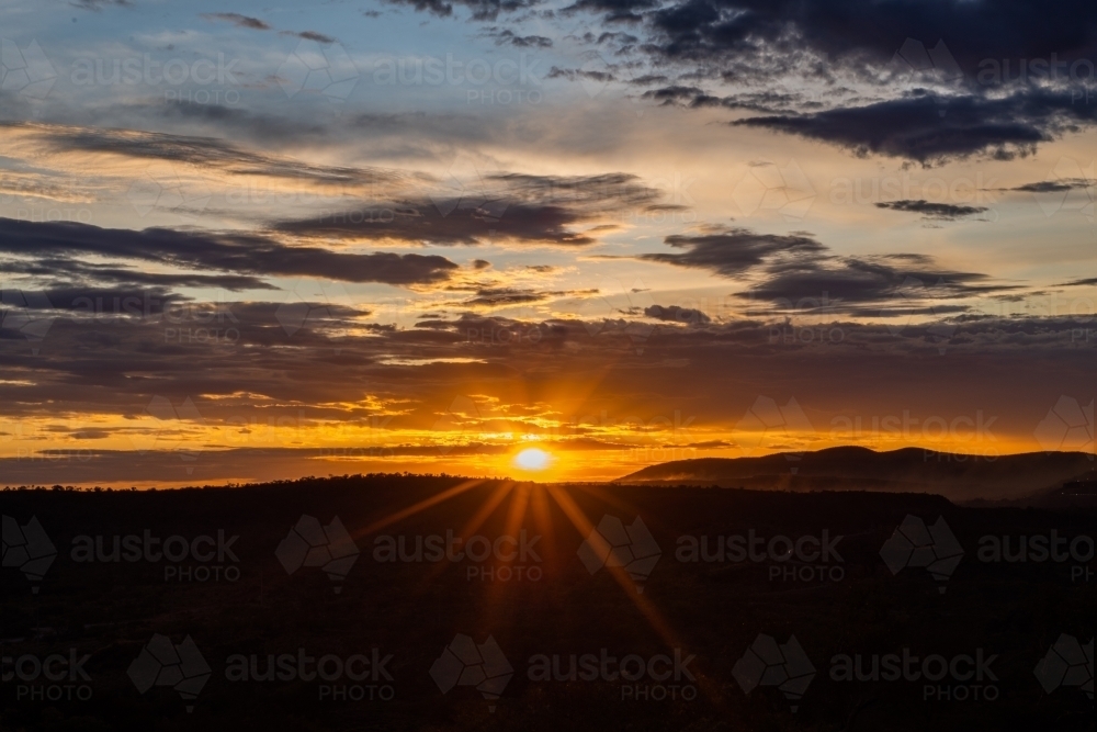 Sun setting in cloudy sky over rural landscape - Australian Stock Image