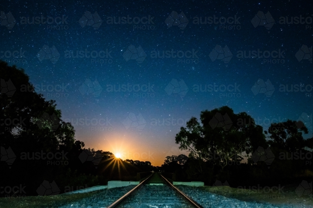 Sun setting over trees from a railway track - Australian Stock Image