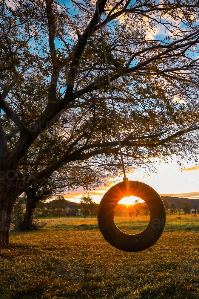 Sun setting through backyard tire swing on country property - Australian Stock Image