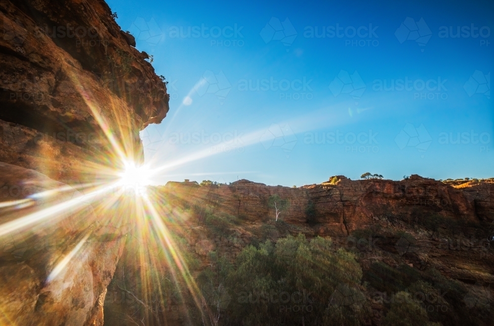 Sun shining past rock at King's canyon in Australia on a blue sky day. - Australian Stock Image