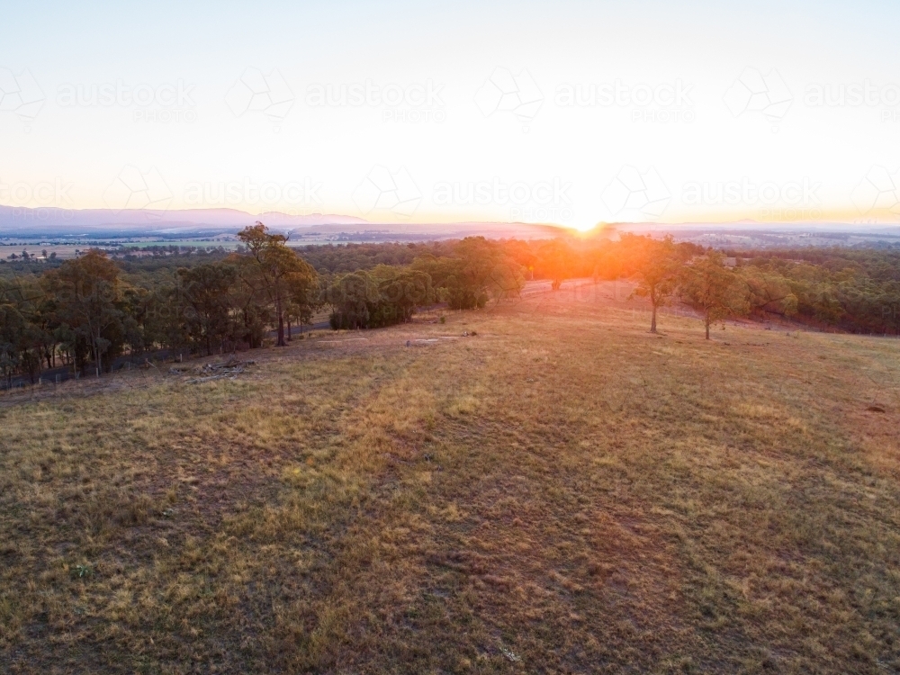 Sun sinking below the horizon of trees and empty paddock - Australian Stock Image