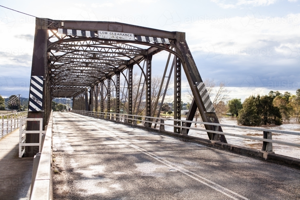 Sunlight over old truss bridge in Singleton with floodwaters rising in river - Australian Stock Image