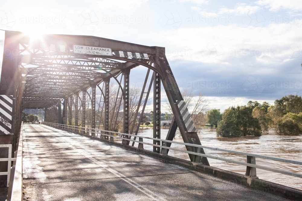 Sunlight over old truss bridge in Singleton with floodwaters rising in river - Australian Stock Image