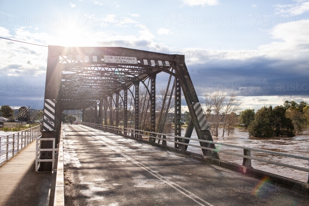 Sunlight over old truss bridge in Singleton with floodwaters rising in river - Australian Stock Image