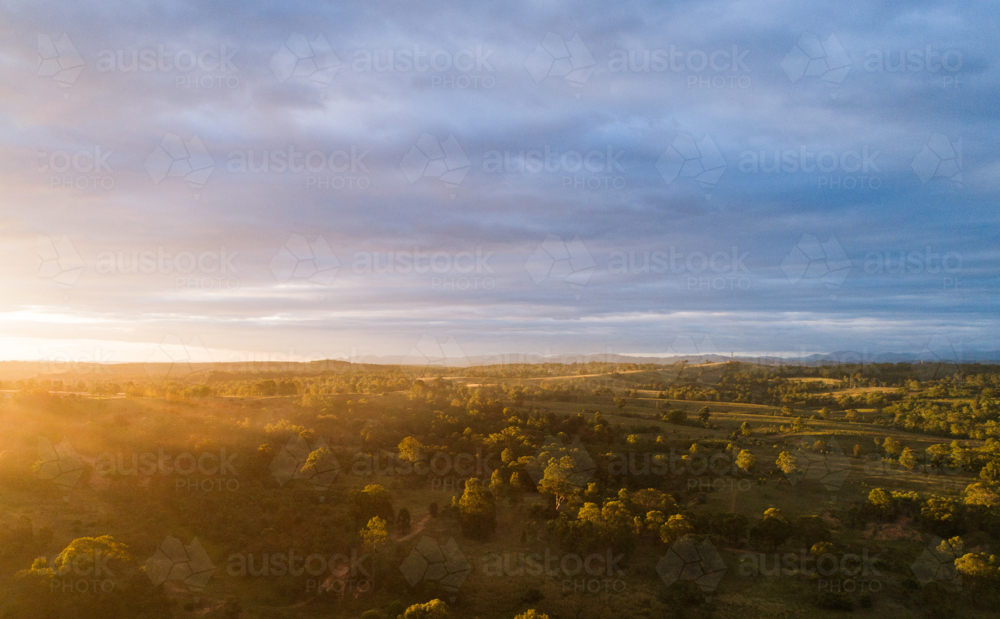 Sunlight peeking from under storm clouds in paddock dotted with gum trees - Australian Stock Image