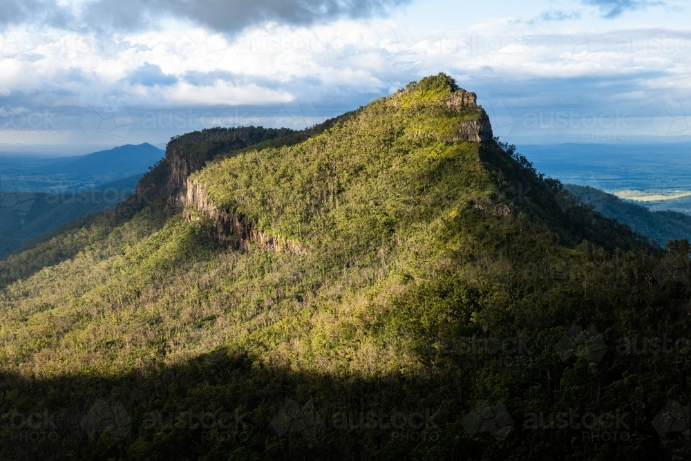 Sunlight piercing through the cloudy sky over the mountain peak. - Australian Stock Image