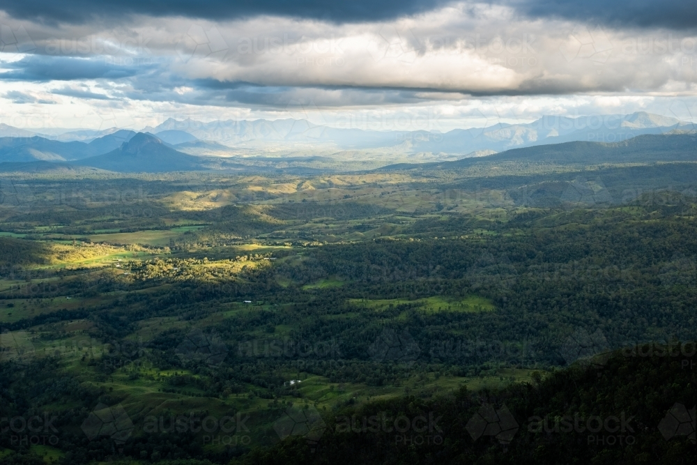 Sunlight piercing through the cloudy sky over the mountainous terrain. - Australian Stock Image