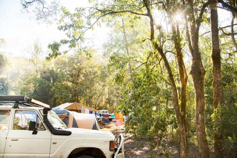 Sunlight through trees at campsite with tents and 4WD - Australian Stock Image