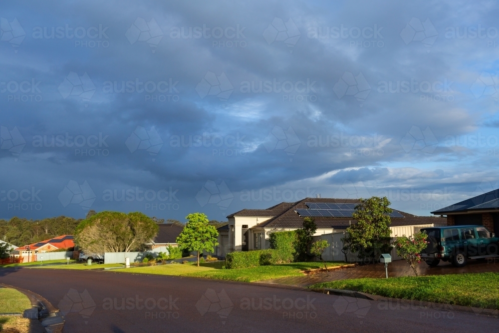 Sunlit suburban street scene fresh after rain with storm clouds in sky - Australian Stock Image