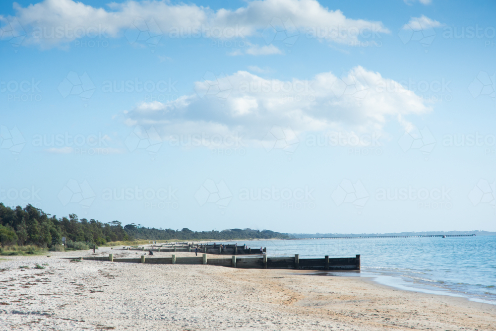 Sunny beach with groynes, blue sky and ocean - Australian Stock Image