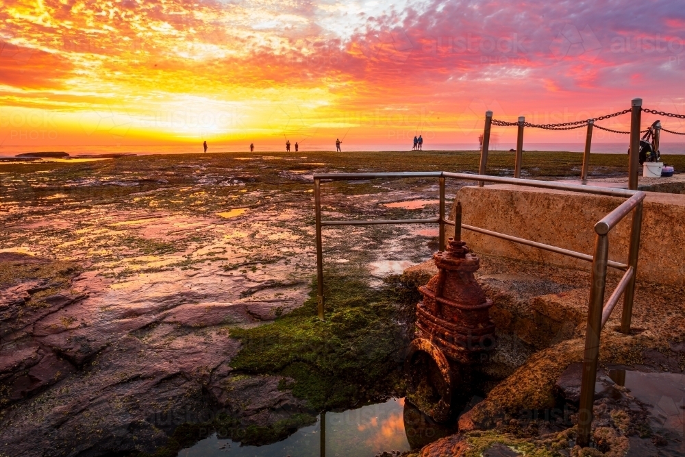 Sunrise and fisherman silhouetted at Mona Vale rock shelf viewed from the edge of the famous rock - Australian Stock Image