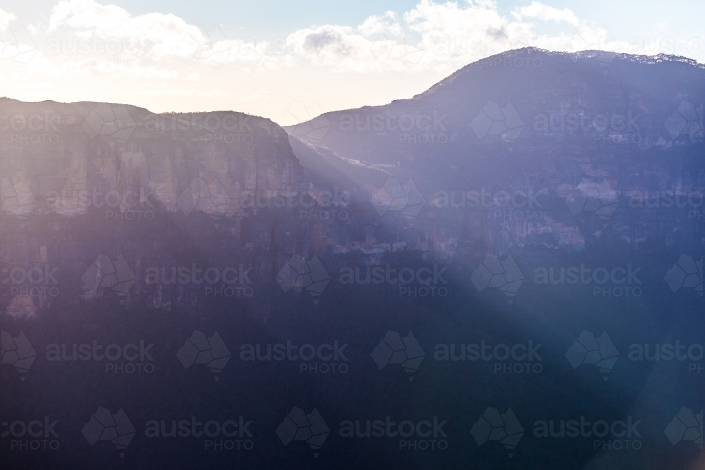 Sunrise beams of light shine over the sandstone cliffs of the Gross valley in the Blue Mountains NP - Australian Stock Image