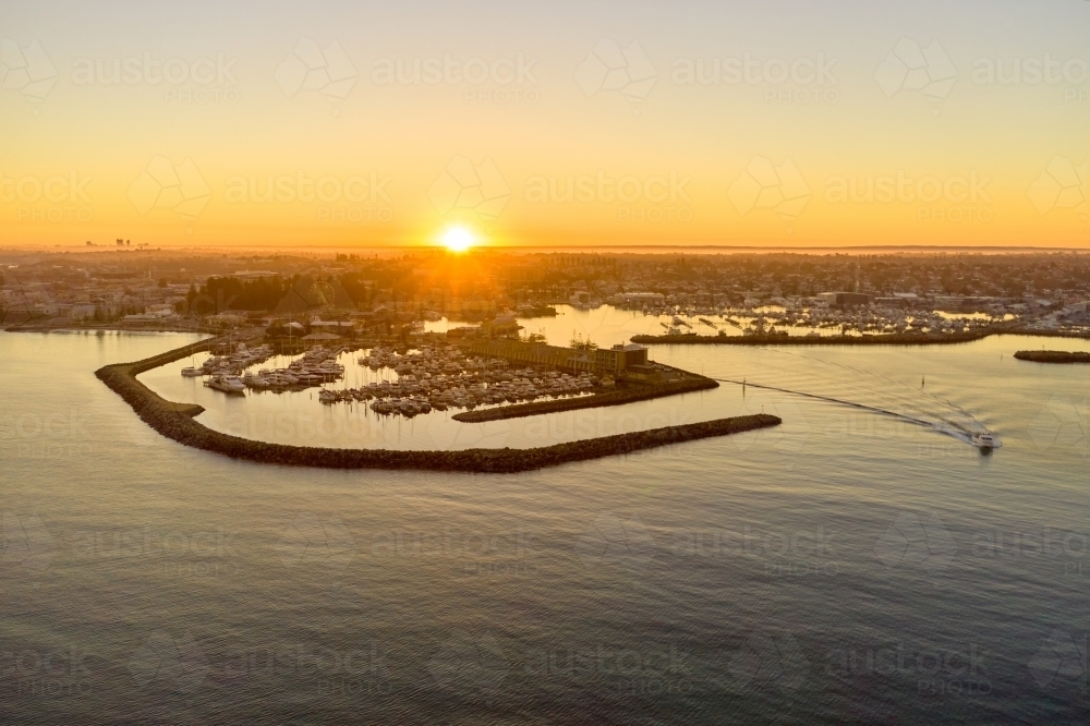 Sunrise on the horizon over Fremantle marina in Western Australia, with a boat leaving the marina - Australian Stock Image