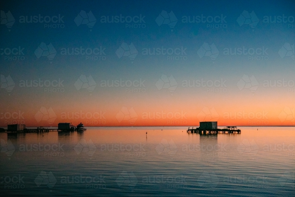 Sunrise over the calm ocean with jetties and fishing shacks - Australian Stock Image