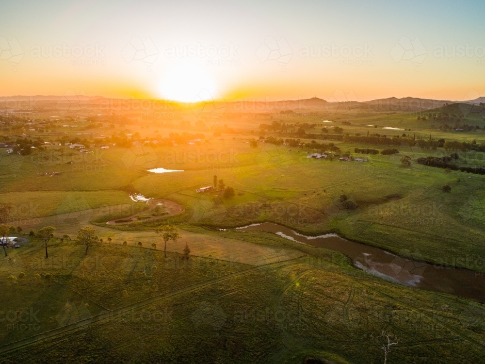 Sunset over valley with dam and creek winding through paddocks of green farmland - Australian Stock Image