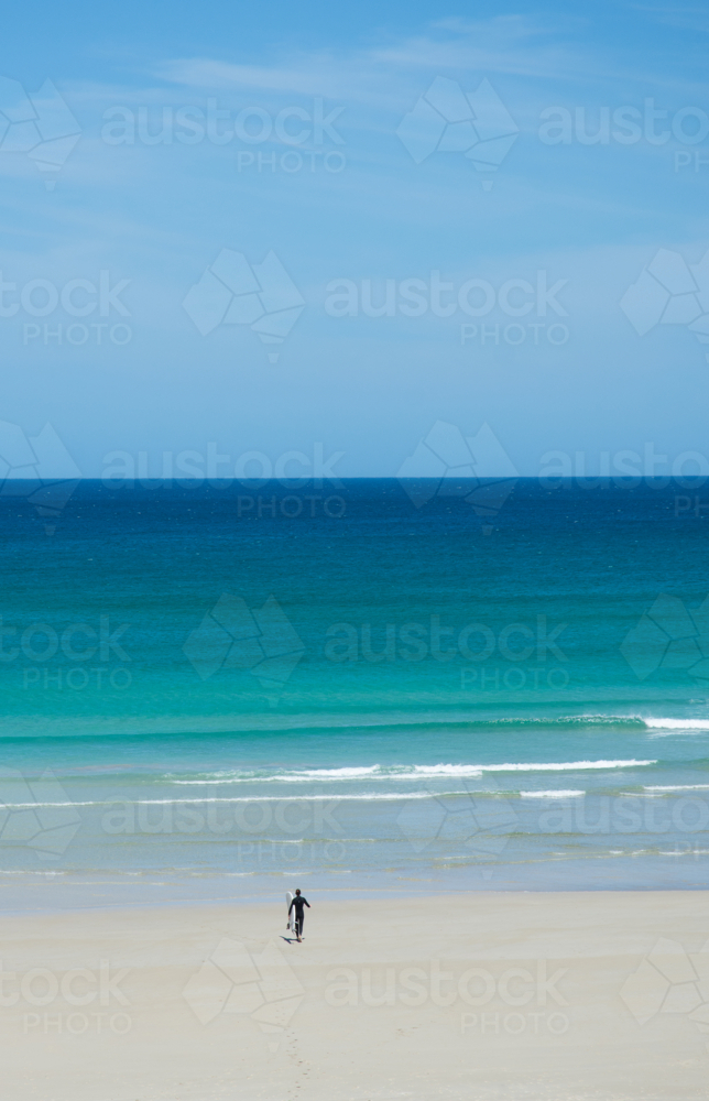 Surfer walking into water on turquoise beach - Australian Stock Image