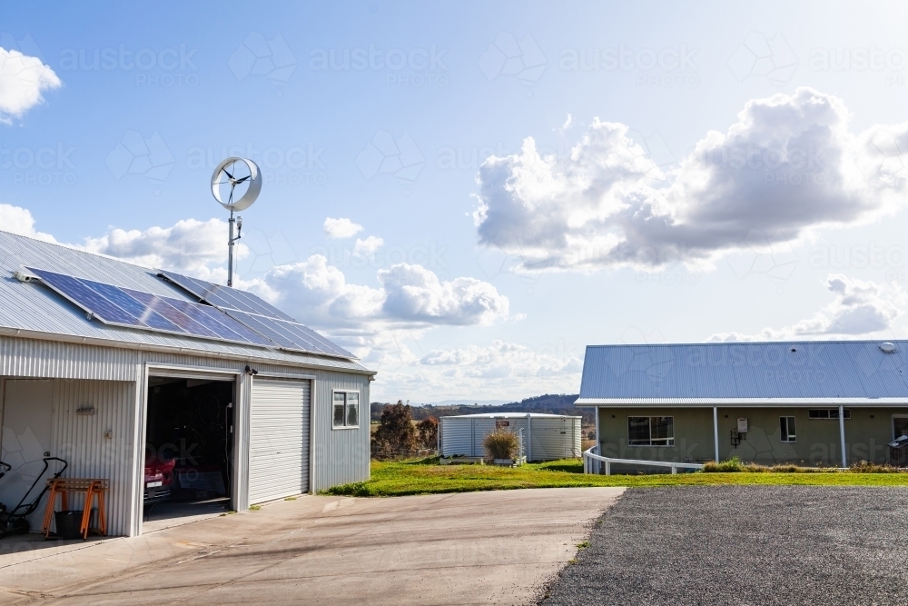 sustainable off grid living with solar power and wind turbine on roof beside farm house - Australian Stock Image