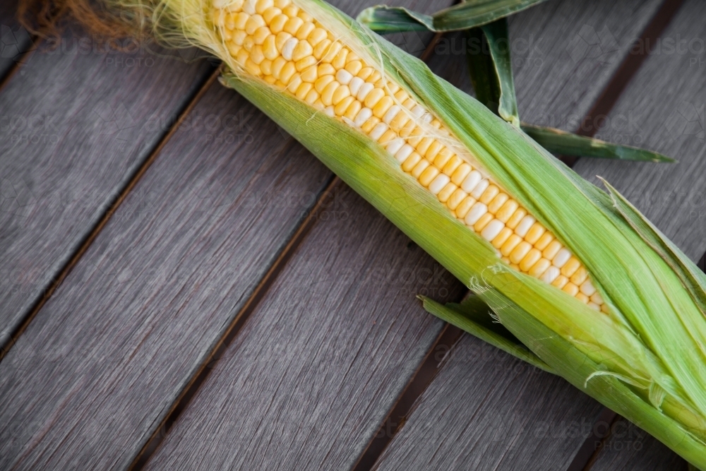 Sweet corn with green husk on wooden table background - Australian Stock Image