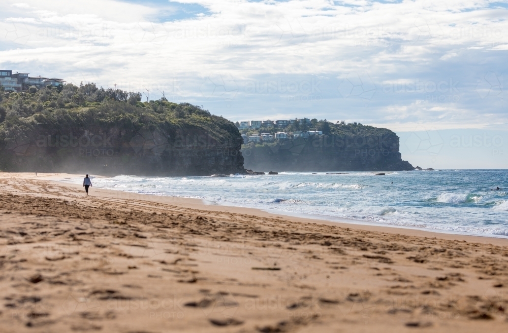 Sydney Beach scene with woman walking in distance towards the cliffs - Australian Stock Image