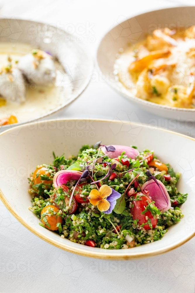 Tabouli quinoa salad topped with edible flowers and red radish. - Australian Stock Image