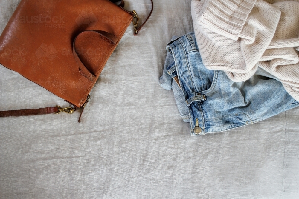 Tan leather bag with jeans and cream woollen jumper on grey linen - Australian Stock Image