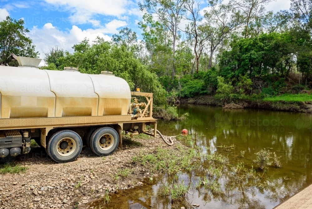 Tanker truck pumping fresh water from a creek next to a concrete flood way - Australian Stock Image