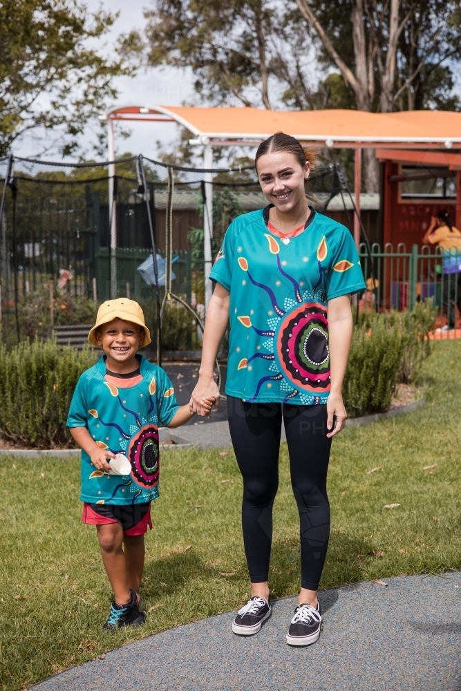 Teacher holding hand on young Aboriginal boy at preschool - Australian Stock Image