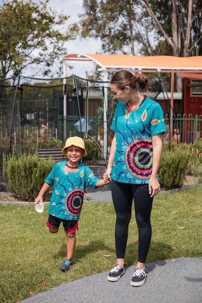 Teacher holding hand on young Aboriginal boy at preschool - Australian Stock Image