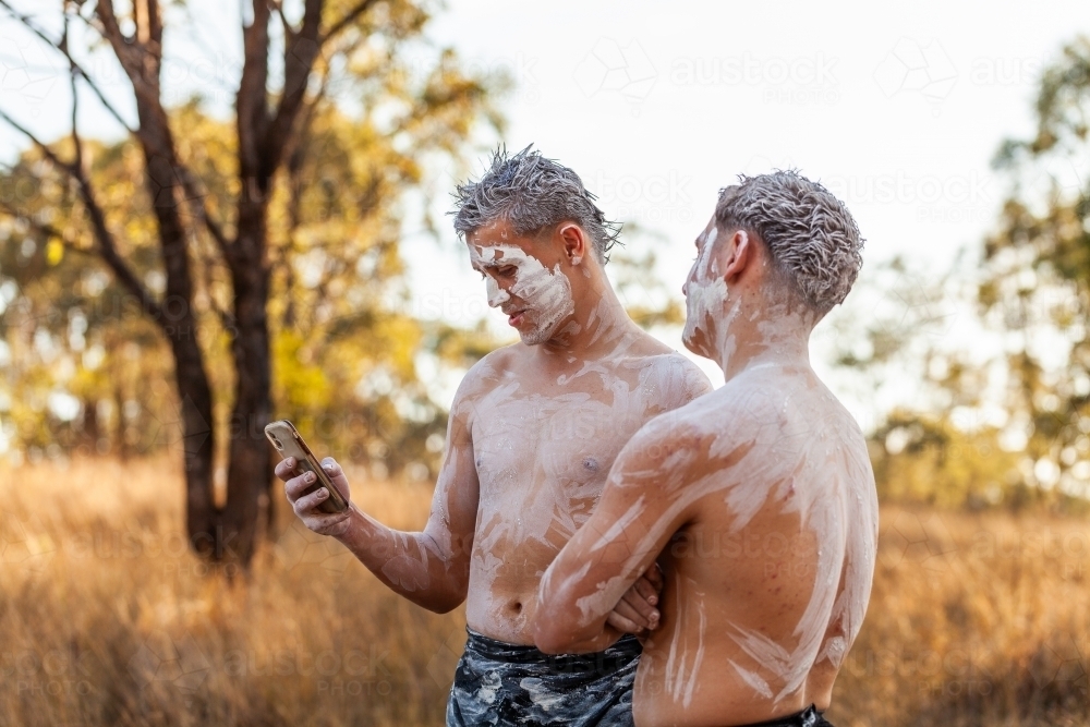 Teen aboriginal cousins in traditional ochre body paint using mobile phone social media - Australian Stock Image