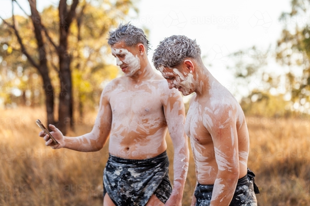 Teen aboriginal cousins in traditional ochre body paint using mobile phone social media - Australian Stock Image