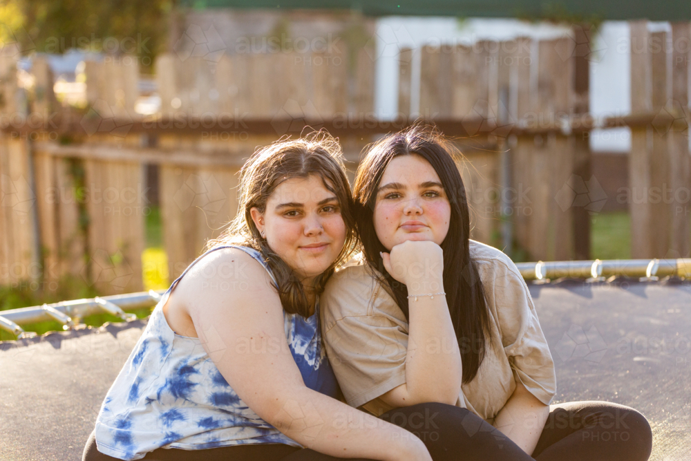 Teen aboriginal sisters sitting together on trampoline in backyard - Australian Stock Image