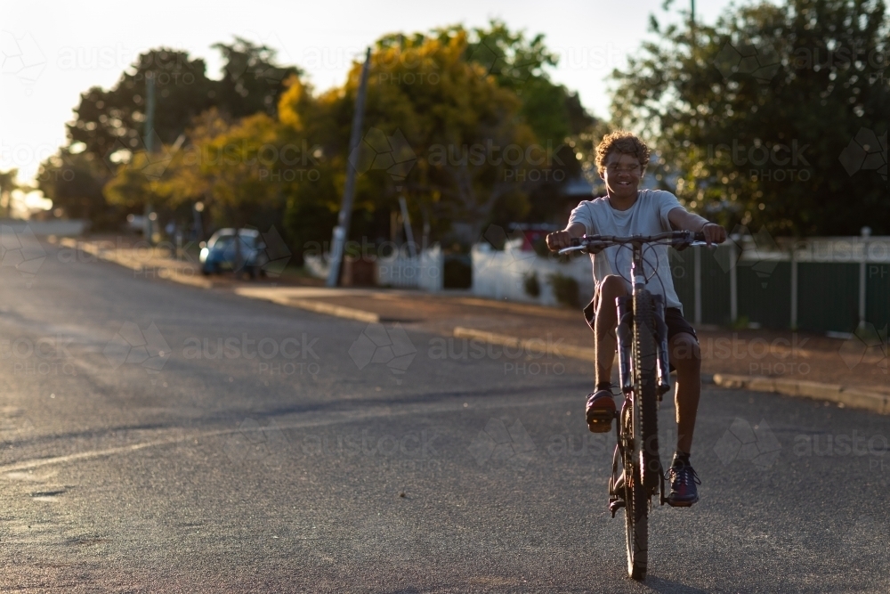 teen boy doing wheelie on bike on quiet street - Australian Stock Image