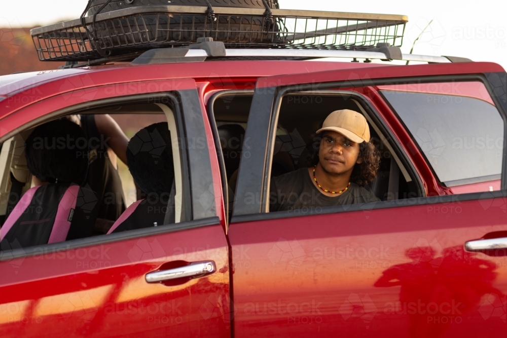 teen boy on back seat of red family car with spare tyre on roof rack - Australian Stock Image