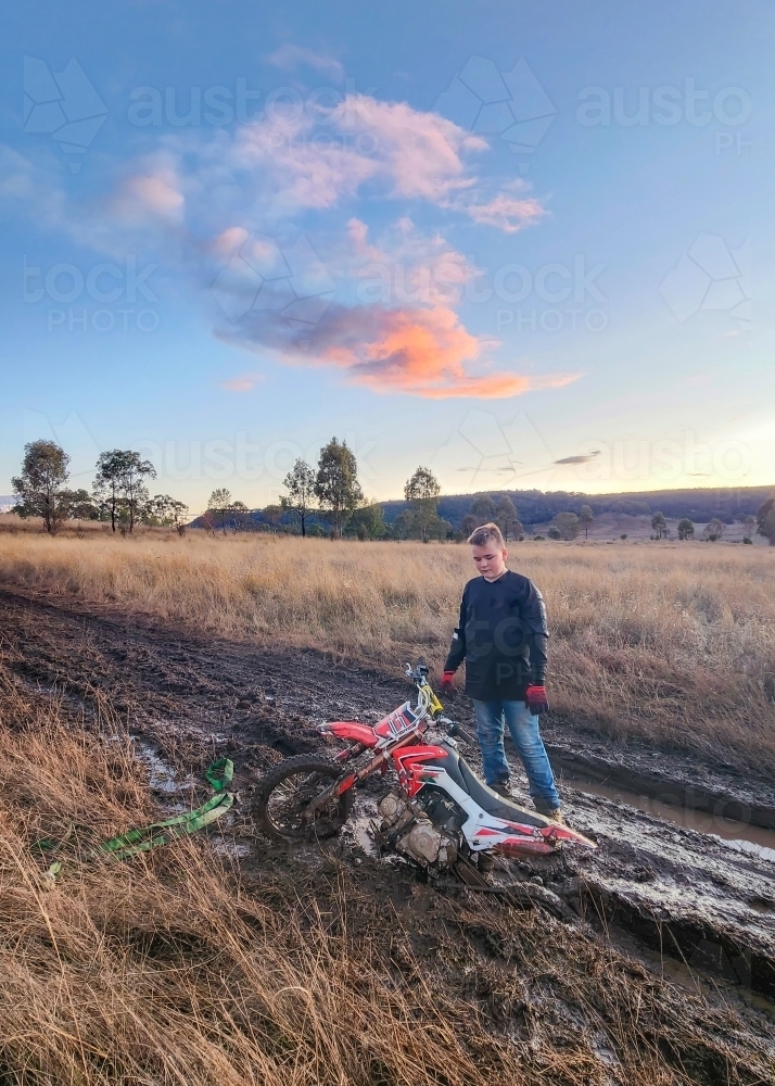 Teen boy on farm with motorbike stuck in the mud - Australian Stock Image