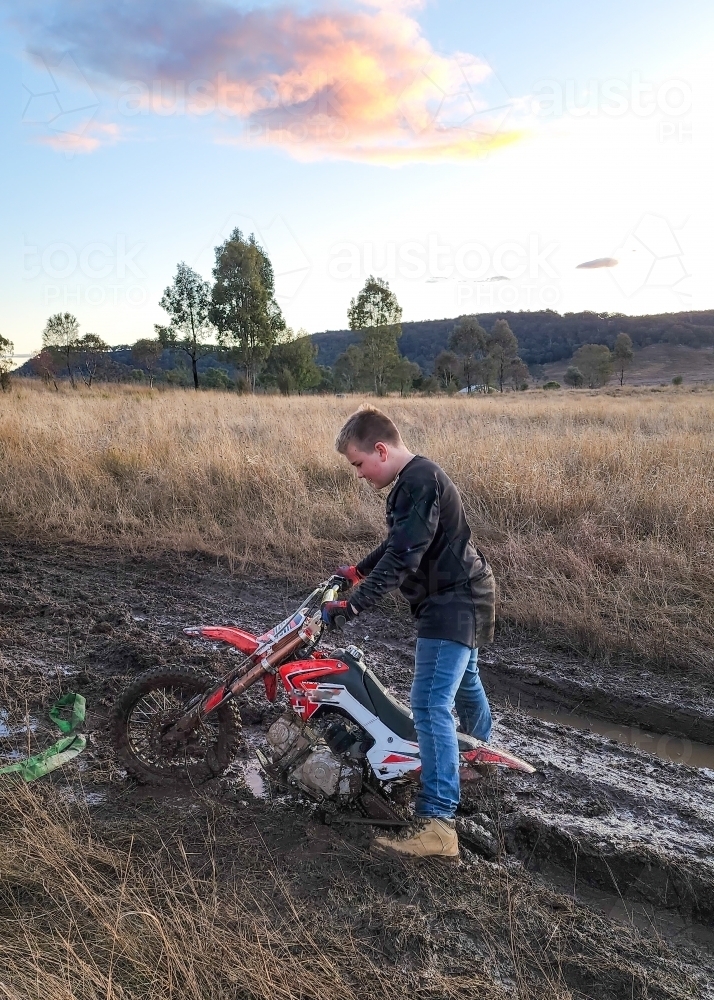 Teen boy on farm with motorbike stuck in the mud - Australian Stock Image