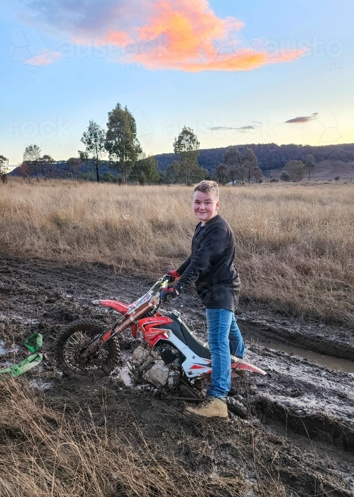 Teen boy on farm with motorbike stuck in the mud - Australian Stock Image