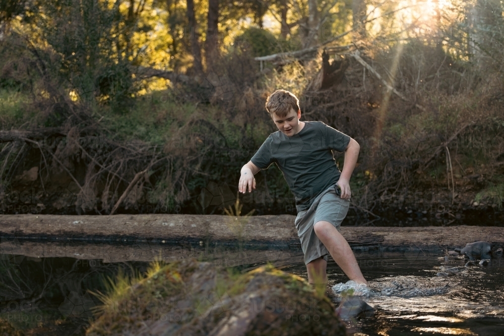 Teen boy walking through shallow creek on nature walk - Australian Stock Image