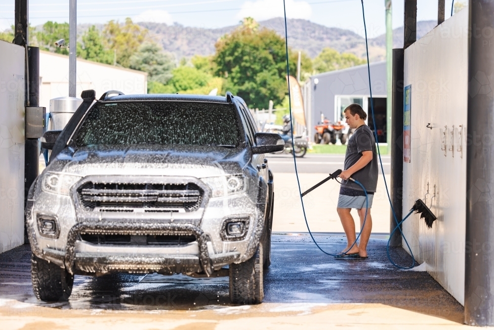 Teen boy washing vehicle in self-service car wash bay - Australian Stock Image